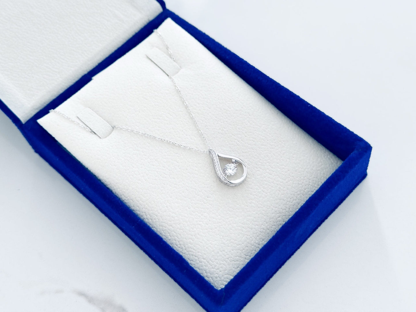 Silver necklace with a teardrop pendant in a blue jewelry box on a white background