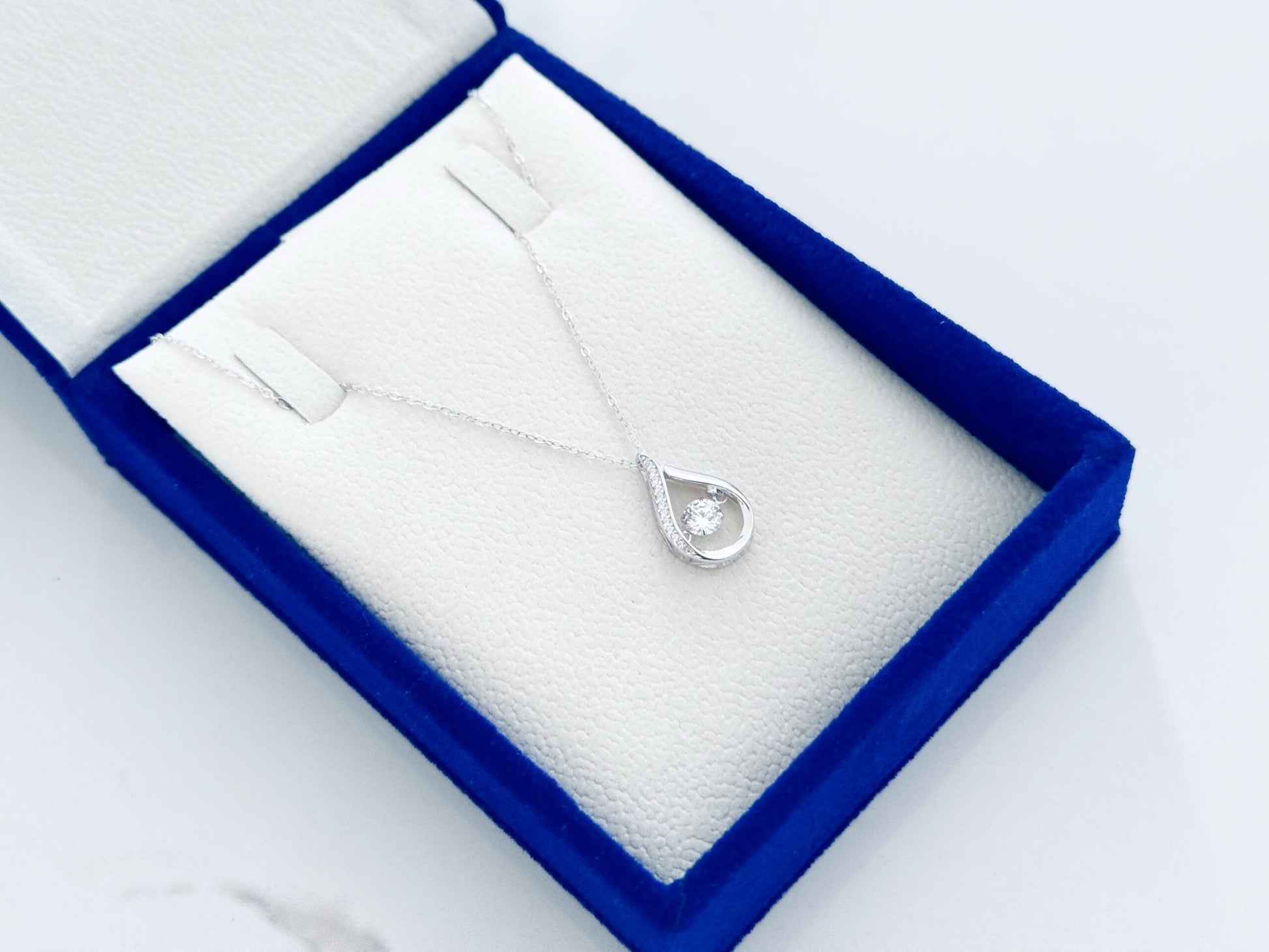 Silver necklace with a teardrop pendant in a blue jewelry box on a white background