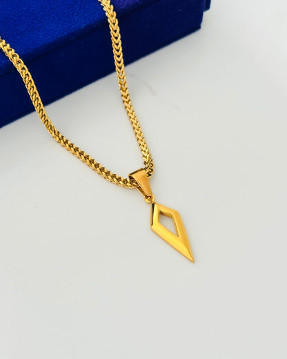 A gold chain necklace with a geometric diamond-shaped pendant, displayed on a white surface with a blue velvet jewelry box in the background.