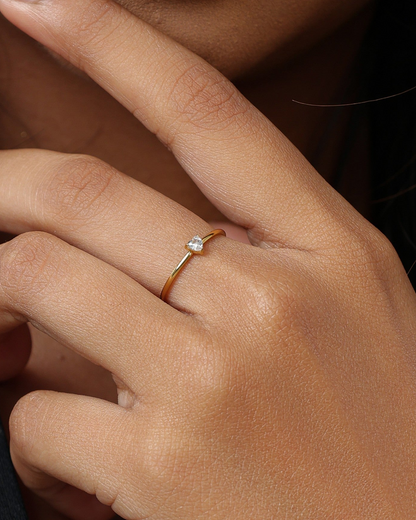 A close-up of a person's hand wearing a delicate gold ring with a single clear gemstone on the ring finger.